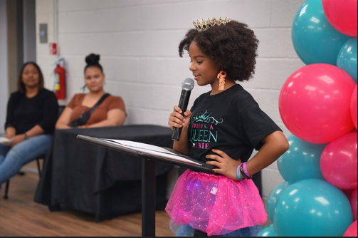 A girl wearing a crown speaks at a lectern during an Enough Period gathering
